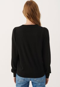 Sort striktrøje med puffede ærmer og en rund halsudskæring, der har en blød tekstur og en tætsiddende kant. Båret med blå jeans.