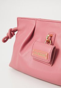 Pink Love Moschino leather handbag with a knotted strap and gold-tone logo plaque on a small front pouch.