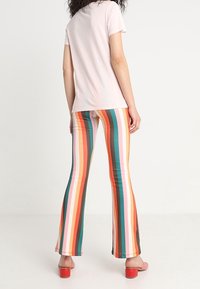 Vista trasera de una persona que lleva una camiseta de manga corta rosa y unos pantalones acampanados de rayas verticales coloridas en tonos naranja, verde y rosa.