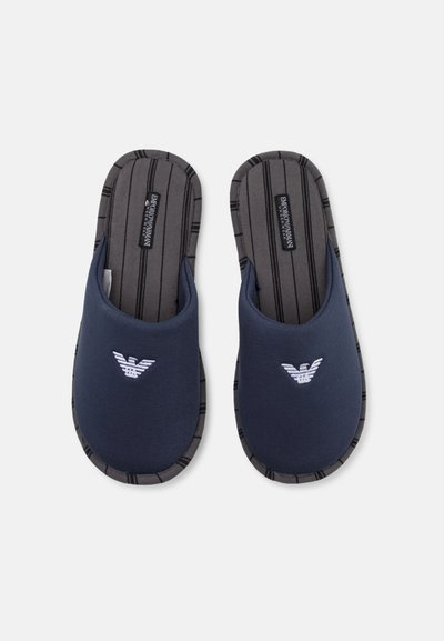 Pantofole blu navy con una morbida tomaia in tessuto, una soletta con righe nere e un logo ricamato nella parte anteriore, con un bordo imbottito.