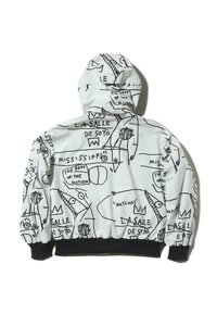 Fehér anyagból készült kapucnis dzseki, fekete absztrakt rajzokkal és szöveggel díszítve. A mandzsetták és az alsó szegély fekete, kiemelve a művészi mintákat.