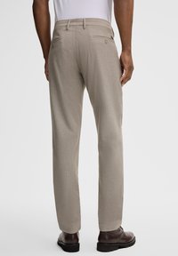 Beige Hosen aus strukturiertem Material mit tailliertem Schnitt, seitlichen Taschen und einer einzelnen Gesäßtasche mit Knopfverschluss.