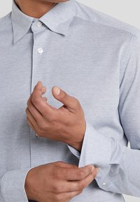 Jasnoniebieska koszula z guzikami, wykonana z teksturowanej tkaniny, ozdobiona drobnym wzorem w jodełkę, z wyłogami i regulowanymi mankietami.