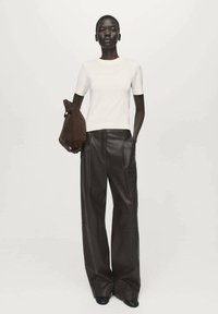 Bela kratka srajca z dolgimi rokavi, kombinirana z ohlapnimi temno rjavimi usnjenimi hlačami. Model drži rjavo torbo z edinstveno obliko.