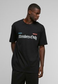 Sort bomulds t-shirt med korte ærmer, der viser "Members Only" i en stiliseret hvid skrifttype, akkompagneret af blå "VENOMOUS" og rød "WORLDWIDE."