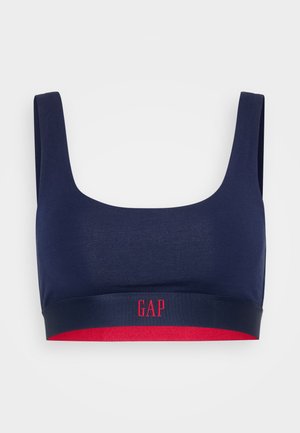 Sostenedor de color azul marino hecho de una tela suave y elástica con escote cuadrado y tirantes anchos. Presenta una banda inferior roja con el logo blanco "GAP".