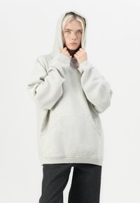 Light gray oversized hoodie made of soft material, featuring a large front pocket and a drawstring hood. Textured fabric with ribbed cuffs.