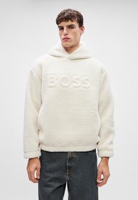 Bijela plišana kapuljača s teksturiranim završetkom, sa reljefnim logotipom "BOSS" sprijeda, u kombinaciji s tamnim trapericama.