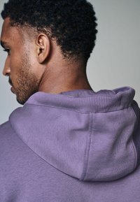 Felpa viola con collo a costine e cappuccio, che mette in mostra una consistenza morbida e un design casual, vista di lato e da dietro.