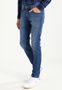 Slim-fit modré denim džínsy s bledým umývaním, klasický dizajn s piatimi vreckami a svetlé švy, doplnené o biele tenisky.