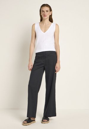 Weißes ärmelloses V-Ausschnitt-Top, kombiniert mit dunkelgrauen weiten Hosen und schwarzen Sandalen mit dicker Sohle. Minimalistisches Design, glatte Textur.