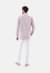 Camicia a maniche lunghe a righe rosse e bianche con colletto classico, polsini abbottonati e vestibilità comoda, abbinata a pantaloni bianchi e scarpe beige.