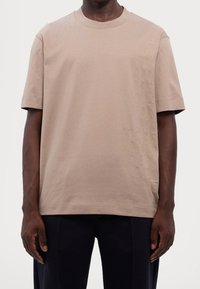 Beige bavlněné tričko s krátkými rukávy, na levé straně s texturovaným vertikálním vzorem. Kulatý výstřih, volnější střih.