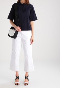 Marinblus i kort modell, vita vida byxor och svarta sandaletter med vita detaljer. Texturerad tyg och knapplist vid kragen.