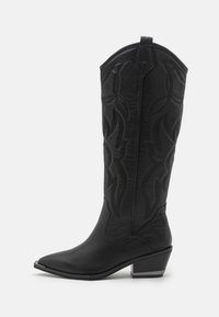 Schwarze Cowboystiefel mit spitzer Zehe, hohem Schaft mit geprägten Blumenmustern und niedrigem Blockabsatz mit metallischem Akzent.