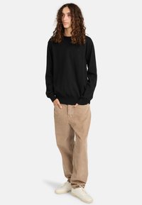 Maglione in cotone nero con collo rotondo e maniche lunghe, abbinato a pantaloni in corduroy beige chiaro e sneaker color crema. Vestibilità rilassata, design semplice.