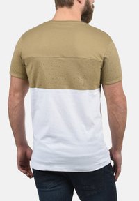 T-shirt med en beige spraglet overdel, der går over til en ensfarvet hvid underdel. Korte ærmer, rund halsudskæring, afslappet pasform.
