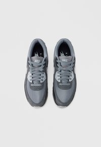 Šedé tenisky Nike z mesh a semišových materiálů. Mají tkaničkový design, polstrovaný límec a bílé logo na bocích.