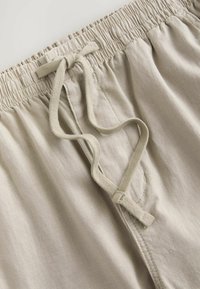 Beige bomulds shorts med elastisk talje og justerbar snor. Har en glat tekstur og syede sider.