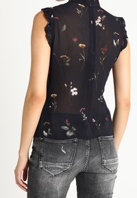 Sheer black blouse with floral print, ruffled shoulders, and a high neckline. Worn with distressed gray denim jeans.