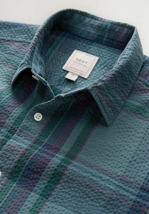 Lühikese varrukaga roheline ruuduline särk, millel on tekstuuriga kangas, valged nööbid ja kraega kaelus. Sildil on kirjas "NEXT, Regular Fit, M."