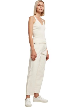 Biała prążkowana koszulka na ramiączkach z dekoltem w serek i szerokimi ramiączkami, zestawiona z beżowymi spodniami o szerokich nogawkach z wysokim stanem i białymi trampkami.