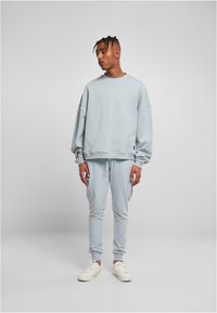 Felpa azzurra chiara con spalle scese, abbinata a joggers coordinati. Misto cotone, texture morbida, vestibilità comoda, con un sottile dettaglio logo.