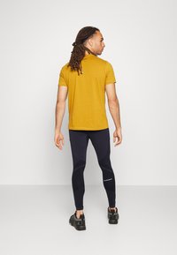 Gul tränings t-shirt med en slim fit, matchad med svarta leggings med geometriska mönster och logotypdetaljer, samt svarta träningsskor.