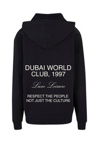 Juoda palaidinė su stilinga kapuce. Tekstas ant nugaros skelbia: "DUBAI WORLD CLUB, 1997 Luxe Leisure" ir "GERBKITE ŽMONES, O NE TIK KULTŪRĄ."
