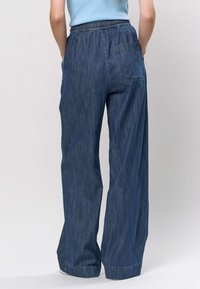 Pantaloni din denim cu croială largă și talie elastică, de culoare albastru mediu, prevăzuți cu un buzunar în spate și o finisare moale, texturată.