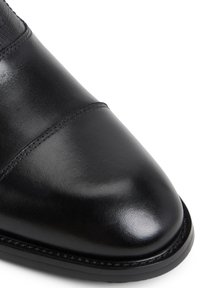 Scarpa in pelle nera con punta arrotondata, texture liscia e dettagli di cucitura sottili nella parte superiore. Suola nera sottile.