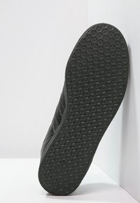 Svart sko sula med ett texturerat, slitbanemönster. Materialet verkar gummiartat med en låg profil. Sidan visar minimal detaljering.