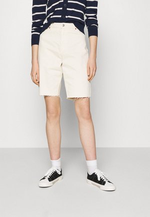 Shorts en denim couleur crème avec des bords effilochés, associés à un cardigan rayé bleu marine et blanc et des baskets noires avec des semelles blanches.