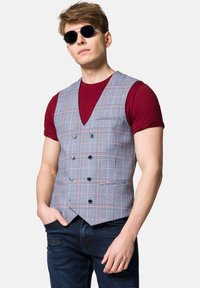 Szary kamizelka w kratę z podwójnym zapięciem, czarnymi guzikami i dwiema kieszeniami, noszona na bordowej koszulce. Model ma także na sobie okulary przeciwsłoneczne.