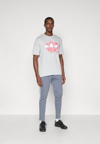 Γκρι κοντομάνικο μπλουζάκι με φωτεινό ροζ γραφικό σχέδιο και γκρι φόρμες με άσπρες ρίγες στο πλάι. Μαύρα αθλητικά παπούτσια ολοκληρώνουν την εμφάνιση.