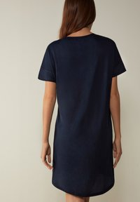 Abito blu navy a maniche corte con una texture morbida, orlo arrotondato e dettagli di cucitura minimi. La vista posteriore mette in evidenza una vestibilità rilassata.