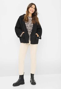 Sort uldfrakke med en afslappet pasform, beige dyreprint sweater, creme corduroy bukser og sorte ankelstøvler med teksturerede såler.
