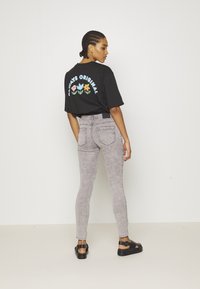 T-shirt preto de manga curta com gráficos coloridos de flores nas costas; combinado com jeans skinny cinza claro e sandálias pretas baixas.