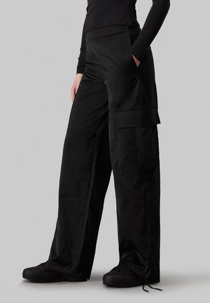 Black cargo pants with a relaxed fit, featuring side pockets and a drawstring hem. Made from a smooth, matte fabric.