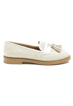 Beigenvärinen kudottu loafer-kengän tyyppinen kenkä, jossa on ruskea pohja, valkoinen nahkainen remmi ja kaksi vastaavaa tupsua päällä.