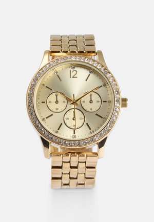 Goldfarbene Uhr mit rundem Ziffernblatt, drei Hilfszifferblättern und einem mit Strasssteinen besetzten Gehäuse. Das Metallarmband hat eine polierte Oberfläche.