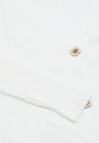 Weißer strukturierter Cardigan mit Fischgrätmuster, gerippten Bündchen und einem hellbraunen Knopfdetail auf der Vorderseite.