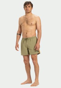 Zelené plavecké šortky s textúrovanou tkaninou, elastickým pásom a šnúrkou. Bočné detaily majú žlté pruhy a malú logovú nášivku.