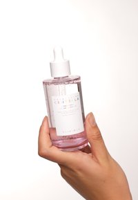 Klar glasflaska med en vit pipettkork som innehåller en ljusrosa vätska. Etiketten har texten "Madagascar Centella" och produktinformation.