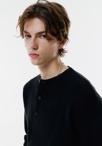 Tricou henley negru din tricot, cu trei nasturi la guler, având un material texturat și un design ajustat. Colier din argint vizibil.