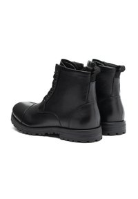 Botas de tobillo de cuero negro con punta redondeada, cierre con cordones en la parte delantera, tirador y suela de goma resistente. Acabados suaves y texturizados, con un detallado minimalista.
