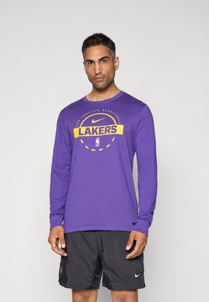 Chemise à manches longues violette avec le logo "Lakers" en jaune ; en coton, avec un col rond, assortie à un short noir arborant un petit logo.