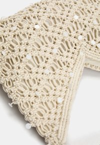 Crèmekleurige geweven katoenen accessoire met een macramé-patroon, versierd met glanzende witte sequins voor extra detail. Textuur- en gestructureerd ontwerp.