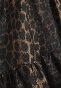 Tissu imprimé léopard marron et noir avec une surface texturée, légèrement brillante et des détails de coutures froncées.