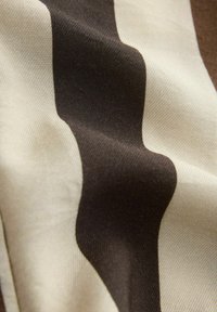 Gros plan sur un tissu avec un motif rayé ondulé alternant des couleurs marron foncé et beige.